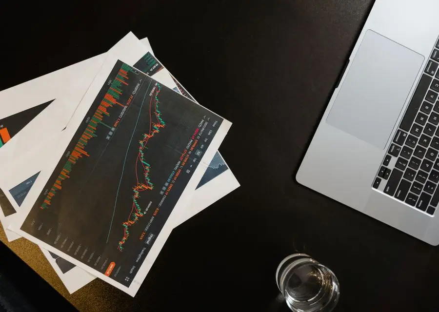 Financial charts and a laptop on a dark desk — the monthly attribution review